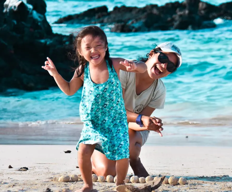 Mother And Young Daughter Laughing Together On A White Sandy Beach In The Galapagos Islands