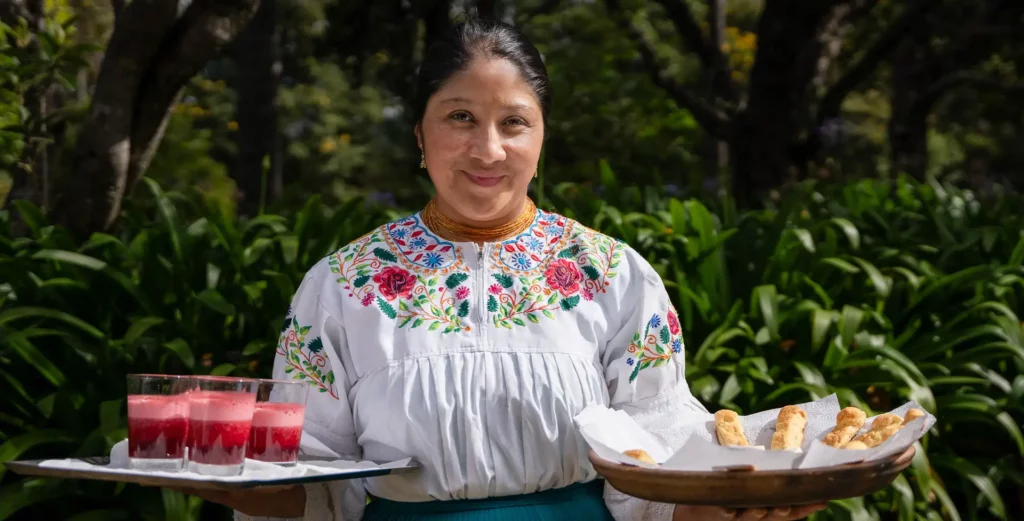 Host in an embroidered blouse serving drinks in the gardens of Hacienda La Compañía