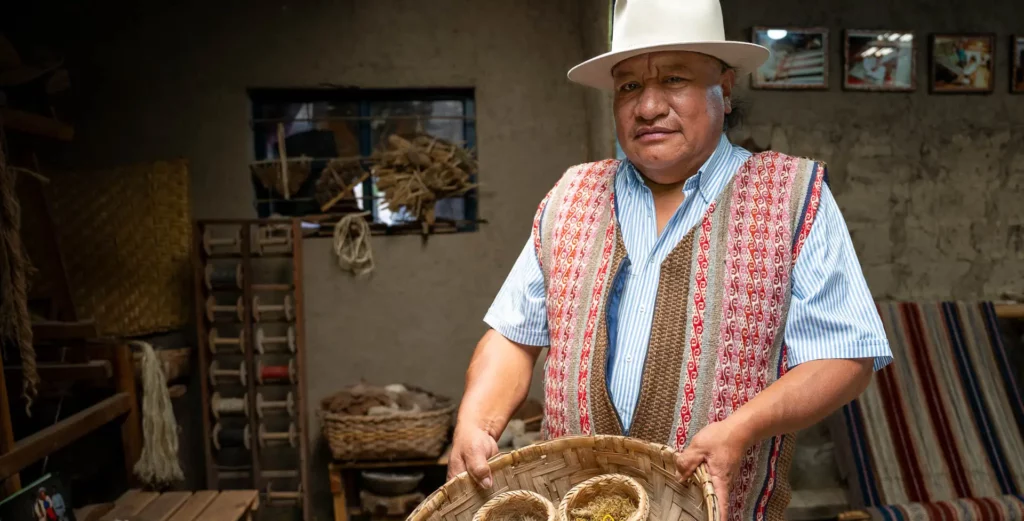 Otavalo artisan holding a basket of hand-spun yarn in his weaving workshop