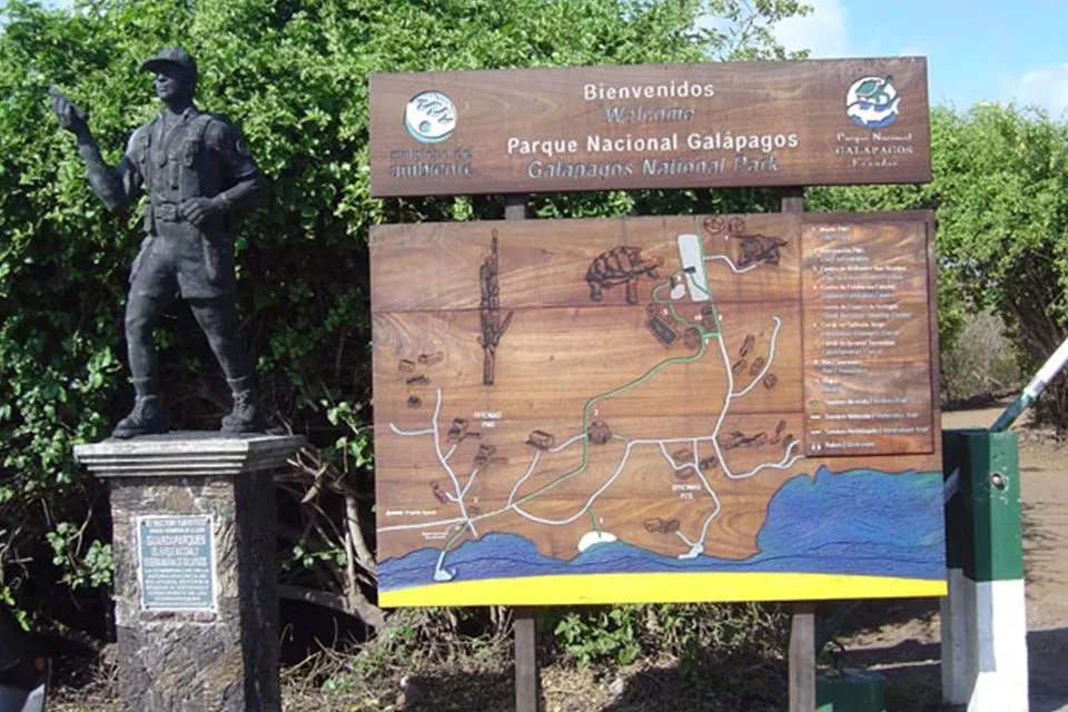 Welcome Sign And Wooden Map At The Entrance Of The Galapagos National Park With A Park Ranger Statue.