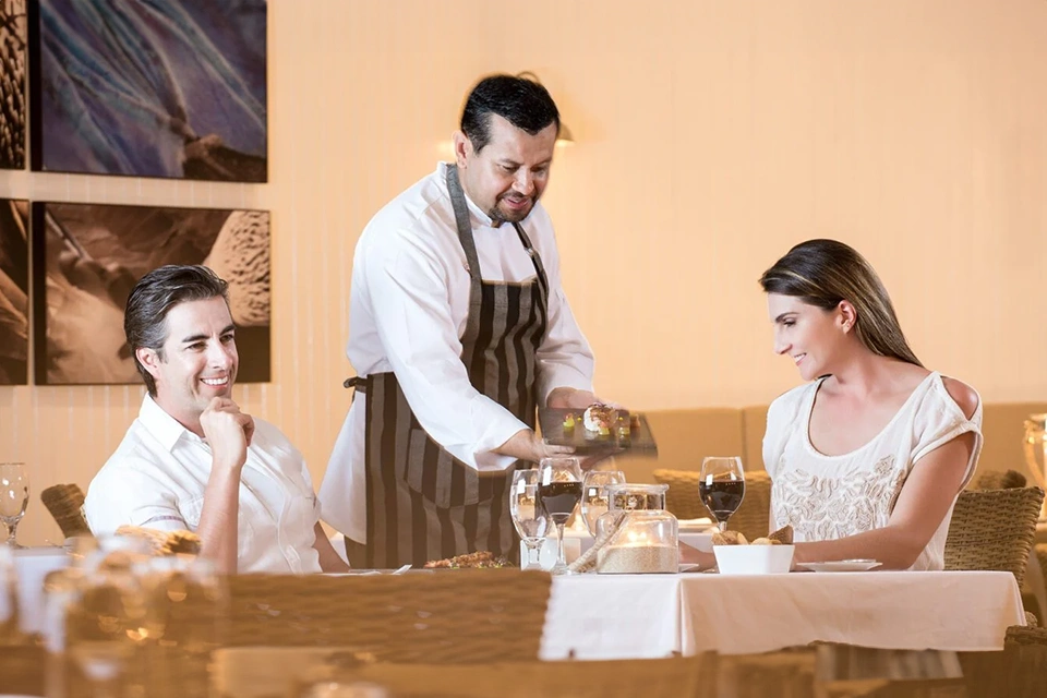 A Couple Enjoying A Fine Dining Experience At The Finch Bay Restaurant In The Galapagos, Being Served By A Professional Waiter.