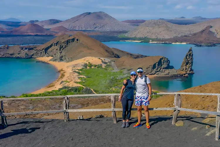 Galapagos northeastern cruise — couple at Bartolome Island summit viewpoint with Pinnacle Rock and turquoise bay