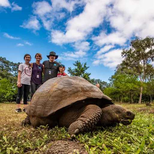 Family Posing Behind A Giant Galapagos Tortoise In A Natural Reserve On Santa Cruz Island