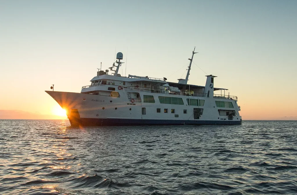 Galápagos cruise ship sailing at sunset with golden light reflecting on the ocean.