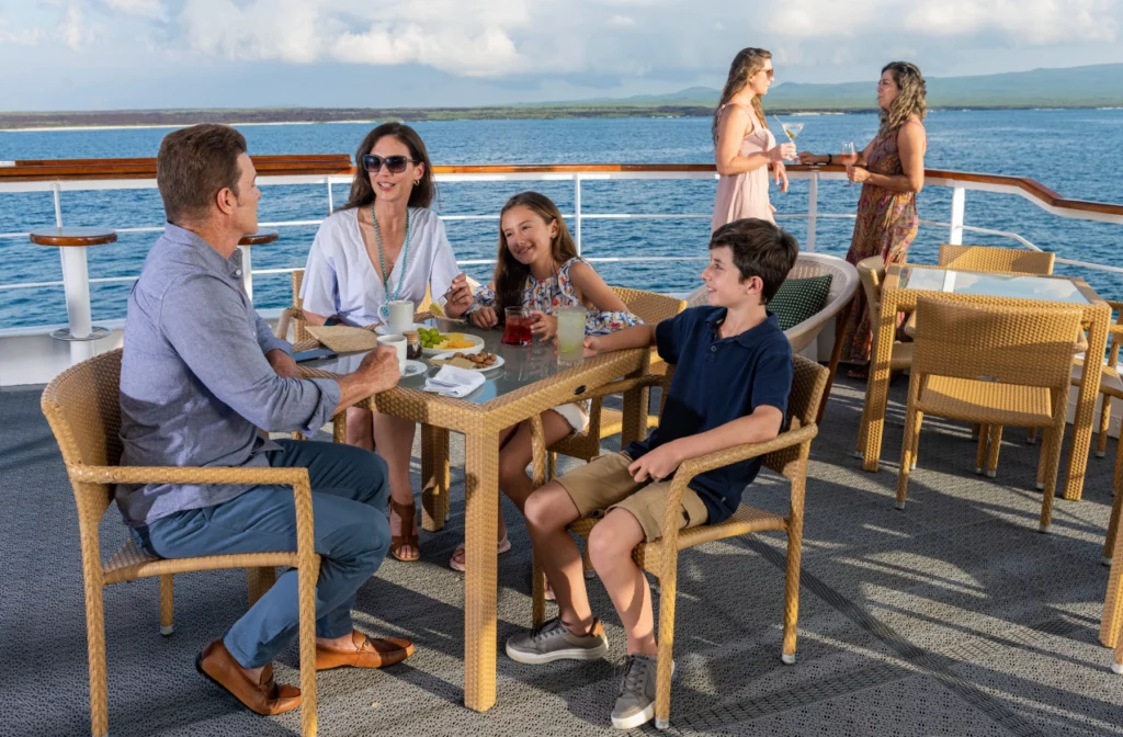 Cena familiar en una mesa de terraza al aire libre con la costa de las Islas Galápagos de fondo a bordo del yate La Pinta.