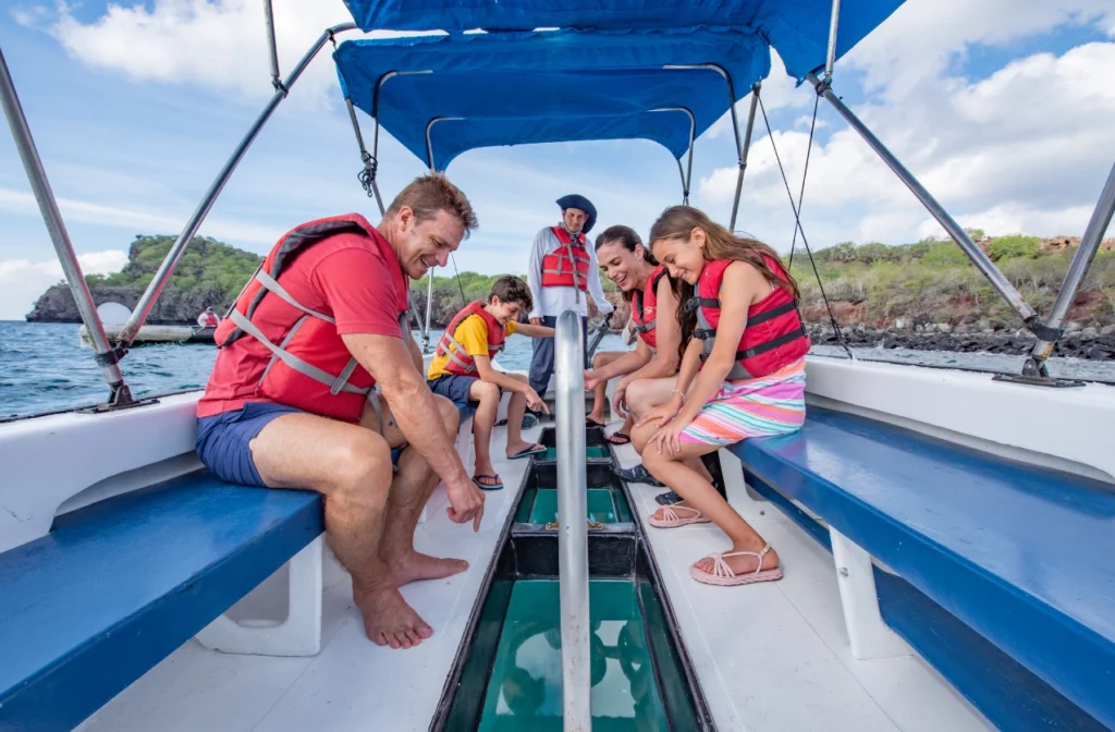 Familia con niños observando la vida marina a través del panel de observación de un barco con fondo de cristal, Islas Galápagos