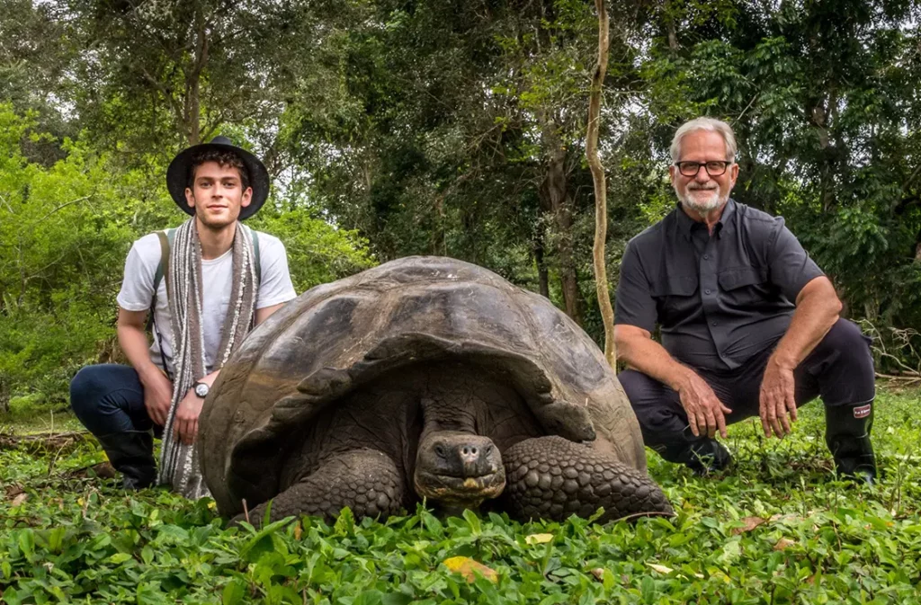 Two guests posing with a Galapagos giant tortoise in the lush highlands reserve, Santa Cruz Island
