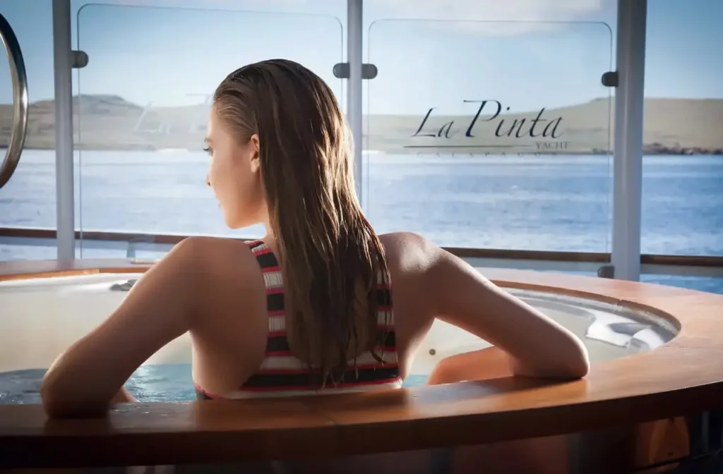 Huésped relajándose en un jacuzzi circular con vistas panorámicas al océano a través de las ventanas a bordo del yate La Pinta.