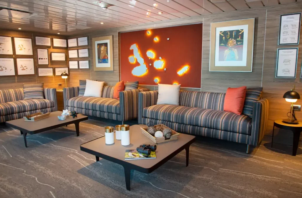 Salón de expedición con sofás a rayas y mapa iluminado de las Islas Galápagos en una pared decorativa a bordo del yate La Pinta.