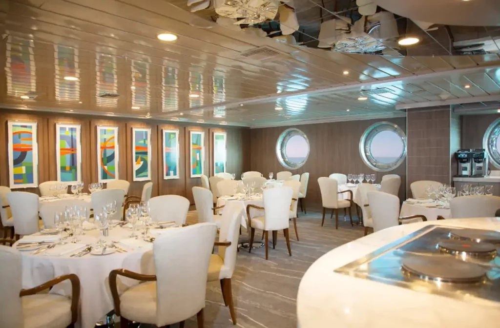 Elegante comedor con mesas redondas, sillones blancos y ventanas tipo ojo de buey a bordo del yate La Pinta.