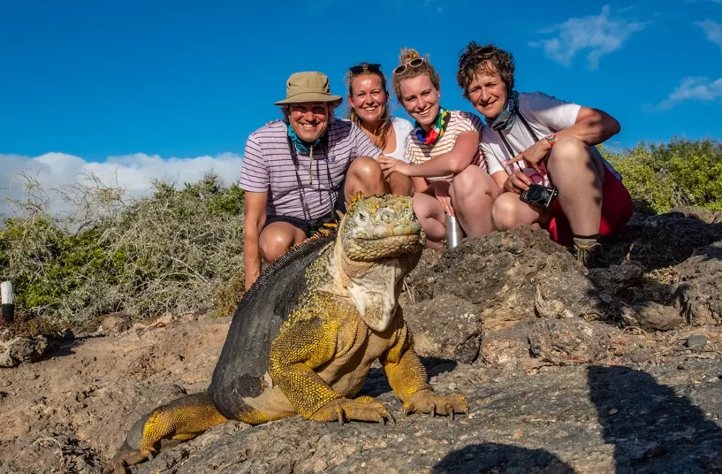 Group of guests posing with a Galapagos land iguana on volcanic rock at South Plaza Island