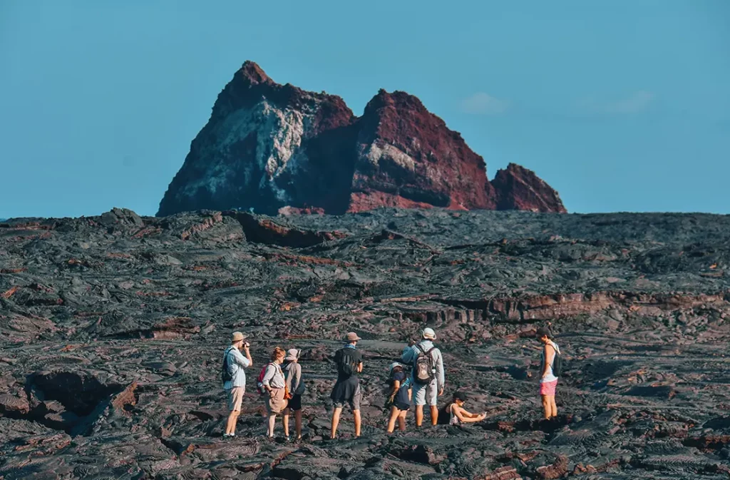 Grupo de expedición caminando por los campos de lava de la bahía de Sullivan con formaciones de roca volcánica roja, Isla Santiago, Galápagos.