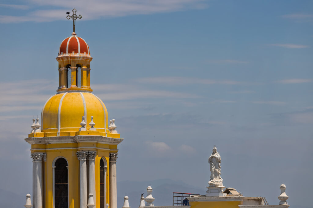 Yellow tower of Chiclayo Cathedral beside a statue of the Virgin in the Main Square.