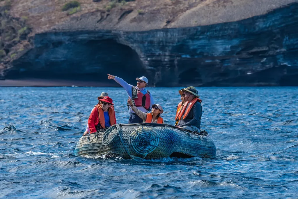 Excursión a Galápagos desde Quito: un guía naturalista señala la fauna desde una lancha cerca de acantilados volcánicos.