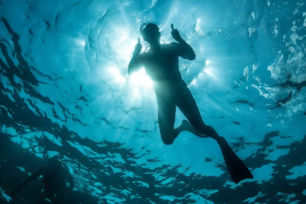 Buzo con esnórquel recortado contra la superficie iluminada por el sol y rodeado de peces, Reserva Marina de Galápagos.