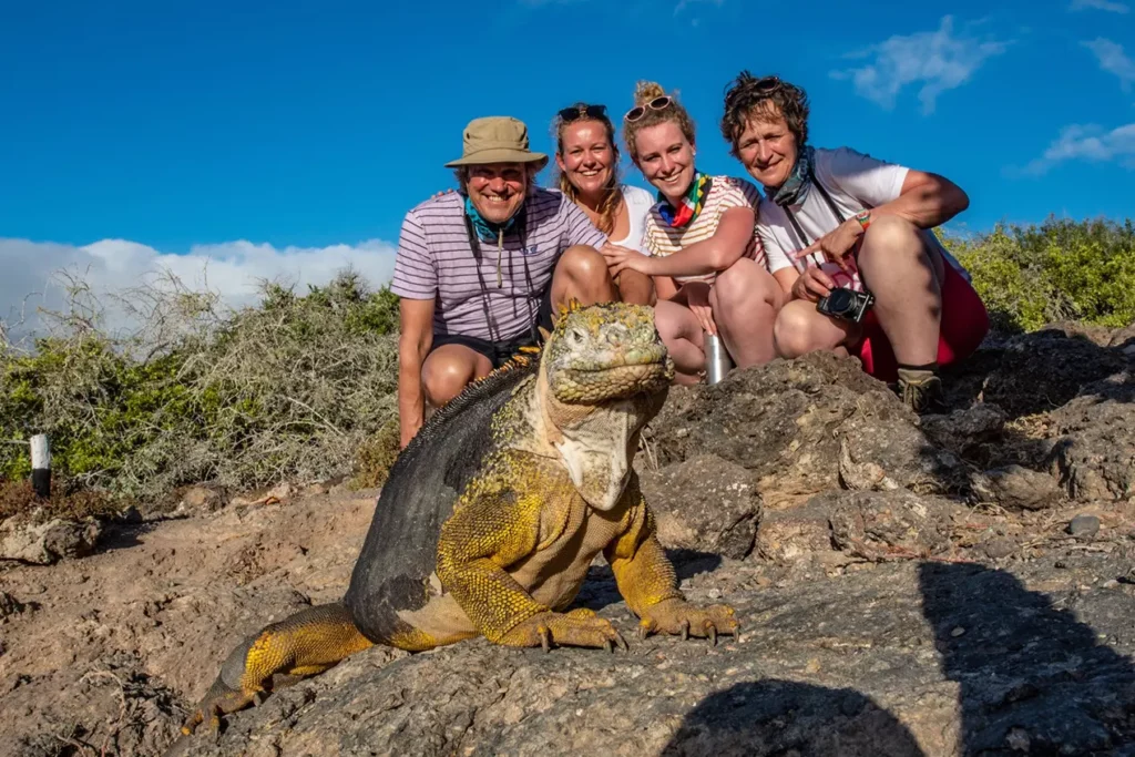 Viajeros posando con iguanas terrestres de Galápagos en terreno rocoso de lava, Isla Plaza Sur.