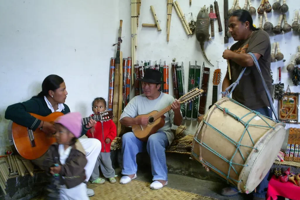 Músicos andinos tocando guitarra y bombo para un pequeño público en Peguche