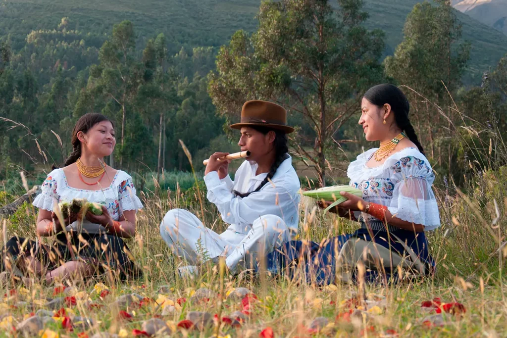 Otavaleños con vestimenta blanca tradicional sentados en un campo de los Andes ecuatorianos