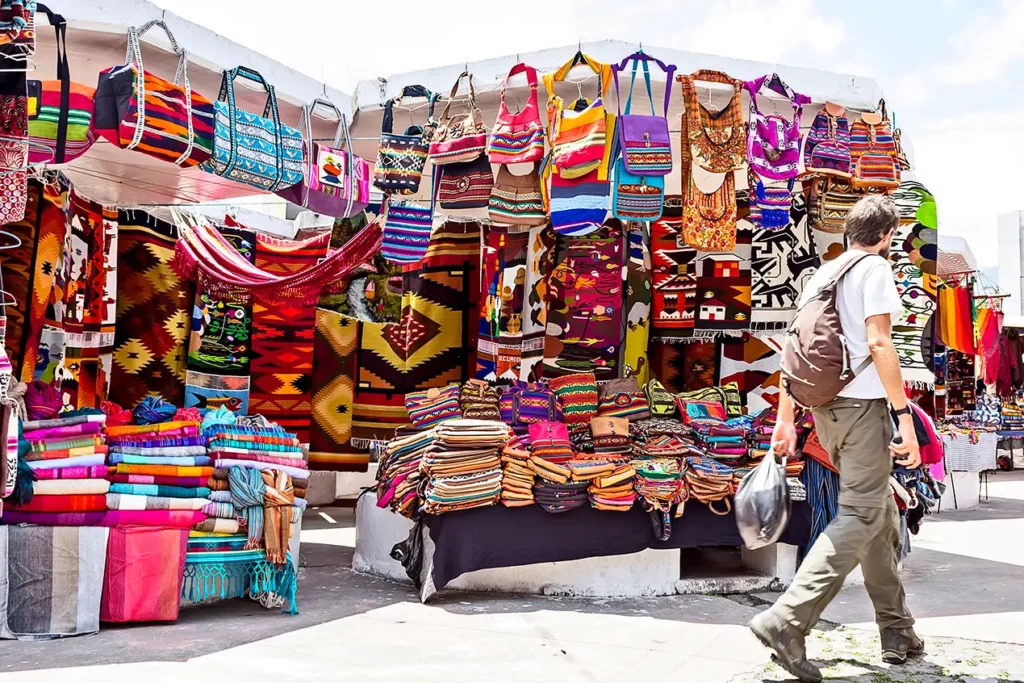 Viajero caminando entre puestos de bolsos y textiles tejidos en Plaza de los Ponchos