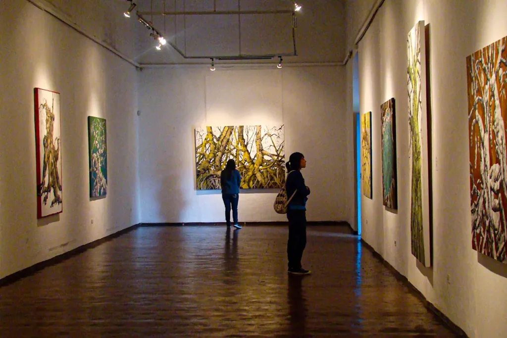 Visitors viewing tree-themed paintings at a modern art gallery in Cuenca