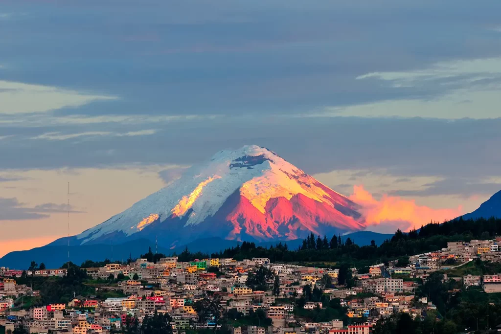 Snow-capped Cotopaxi volcano at sunset over a Quito neighborhood
